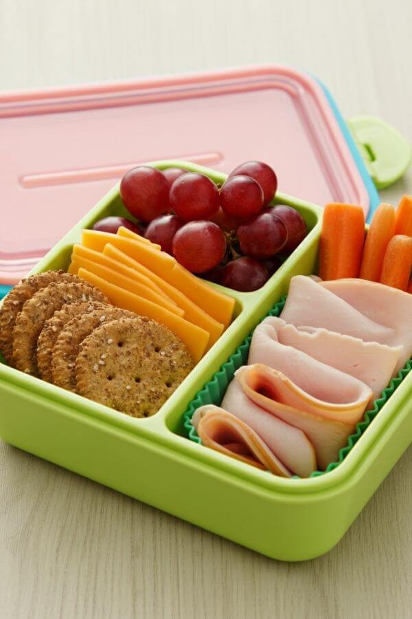 A colorful bento box with neatly arranged whole-grain crackers, cheese slices, turkey slices, and a side of grapes and baby carrots. The setup should look fun and inviting, with vibrant colors and a clean, kid-friendly layout.