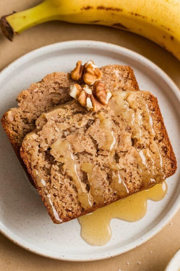 A half loaf of banana bread on a white cutting board, surrounded by scattered slices, bananas, a dollop of Greek yogurt, and a sprinkle of cinnamon. Include a small bowl of chocolate chips or nuts for garnish.