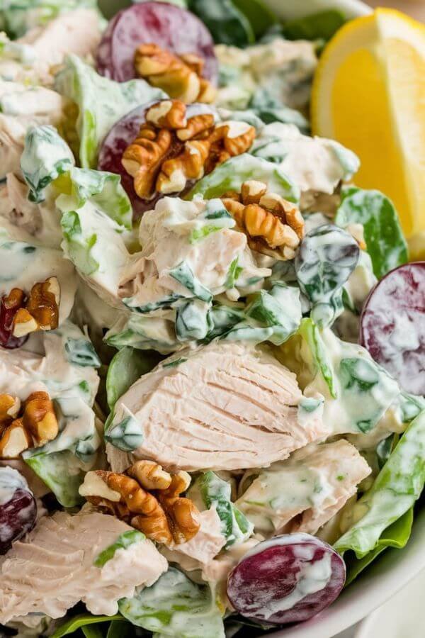 A  close loog of fresh, vibrant chicken salad served in a bowl, garnished with grape halves and walnuts, alongside a lemon wedge. Pair it with a wrap, sandwich, or a plate of greens for a complete, healthy presentation.