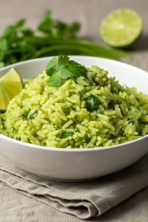 A vibrant bowl of fluffy rice with flecks of green cilantro, served in a white bowl with a lime wedge on the side. Perfectly styled on a neutral tablecloth with fresh herbs and a sliced lime nearby for a fresh, appetizing look.