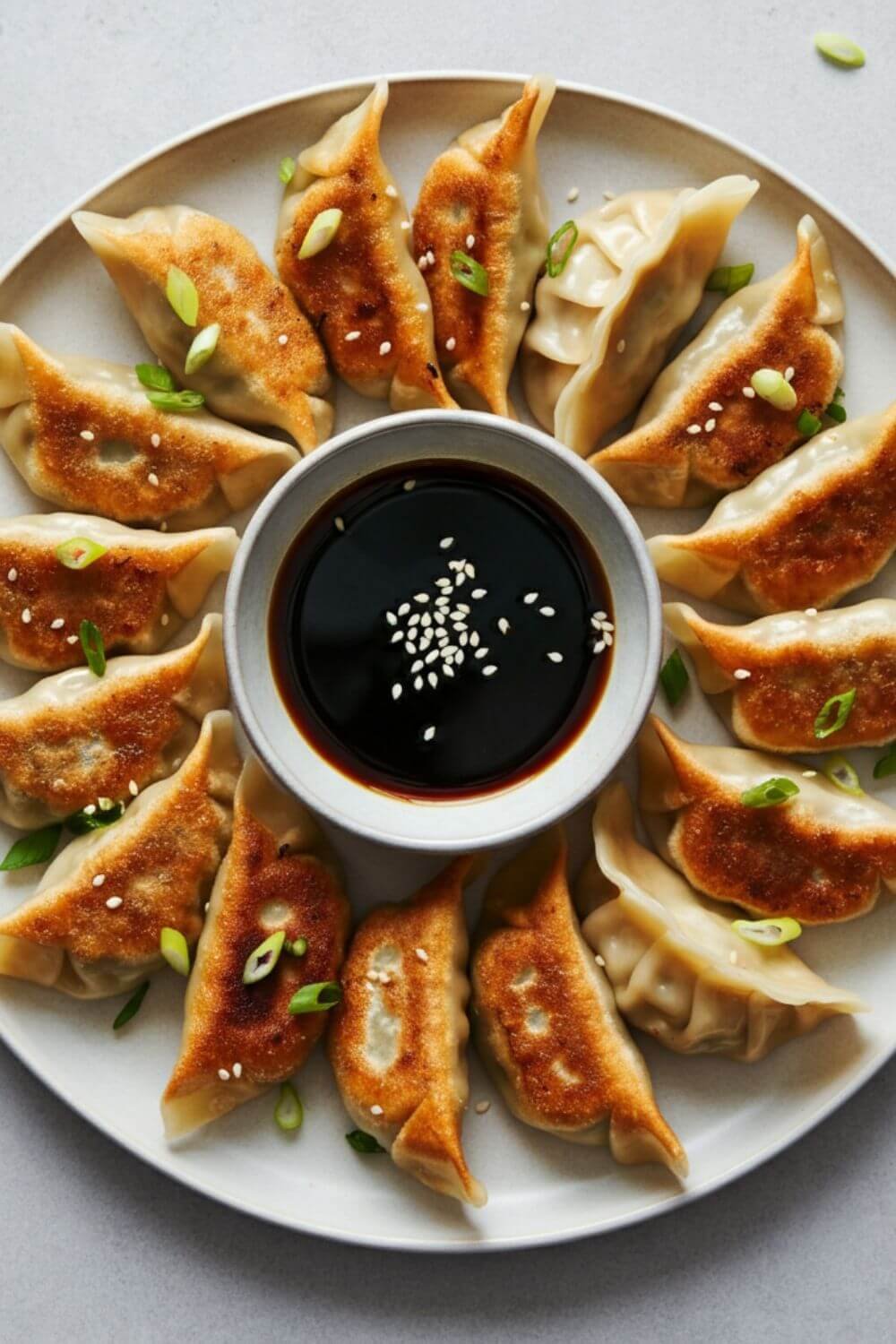 A plate of golden-brown dumplings, some steamed and some pan-fried, arranged neatly with a small bowl of soy-sesame dipping sauce. Garnish with chopped green onions and sesame seeds for a touch of color. the background is light