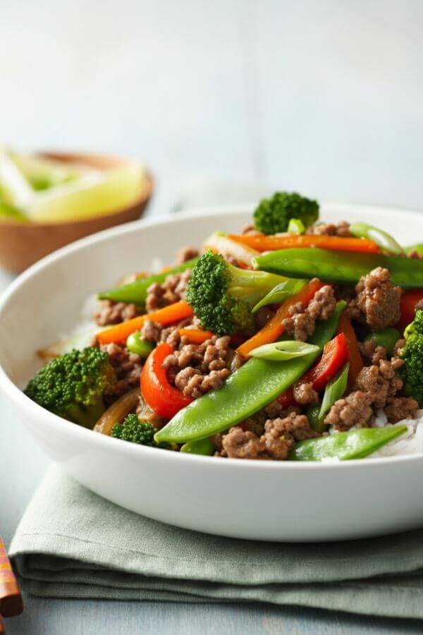 A vibrant stir-fry dish served in a white bowl, featuring perfectly browned ground beef, colorful veggies like broccoli, snap peas, and bell peppers, all glistening with a savory sauce. Pair it with a side of steamed rice or noodles for a complete look!